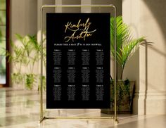 a black and gold wedding seating chart on a stand in front of a wall with potted plants