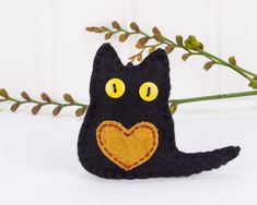 a black cat with yellow eyes and a heart on its nose sitting next to a plant