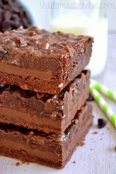 three brownies stacked on top of each other with chocolate chips and milk in the background