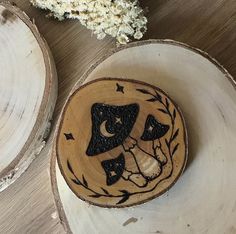 two wooden plates with designs on them sitting on a table next to some dried flowers