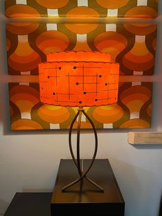 an orange lamp sitting on top of a wooden table next to a wall mounted painting