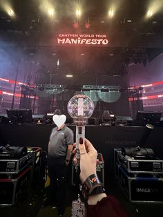 a person holding up a clock in front of a stage with people standing around it