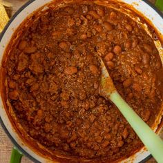 a large pot full of chili and beans with a spatula in the bowl next to it