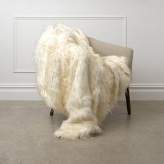 a chair covered in white fur sitting on top of a floor next to a wall