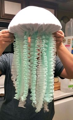 a man is holding up a jellyfish made out of plastic cups and toilet paper