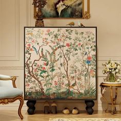 a painting on the wall next to two chairs and a table with flowers in it