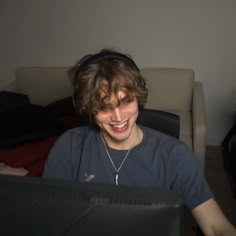 a young man sitting in front of a computer monitor smiling at the camera while wearing headphones