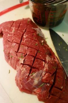 a piece of raw meat sitting on top of a cutting board next to a knife