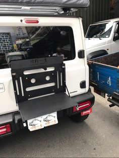 the back end of a white truck parked in front of a blue trailer and other vehicles