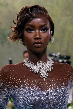 a model wears an elaborate necklace and earrings on the runway