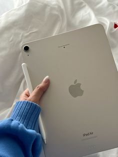 a person holding an ipad in their hand on top of a white sheet covered bed