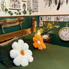 two stuffed animals sitting on top of a bed next to a wall with pictures and clocks