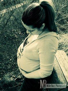 a pregnant woman sitting on a bench in the grass and holding her stomach with both hands