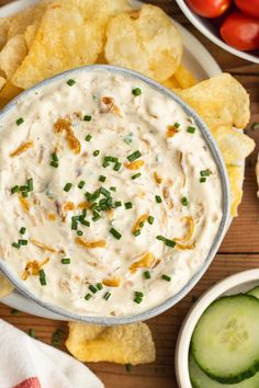 a white bowl filled with dip surrounded by chips and cucumbers