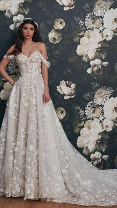 a woman standing in front of a floral wallpaper wearing a white dress with flowers on it