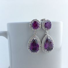 Large purple amethyst cubic zirconia bridal tear drop earrings in rhodium plated brass setting. Earrings feature a large teardrop with pear cut purple amethyst cubic zirconia center surrounded by tiny round zirconia crystals. Teardrop dangles from a earstud with brilliant cut purple amethyst cubic zirconia center and surrounded by tiny round zirconia crystals. This entire halo setting gives a brilliantly beautiful effect. Total length of the earring is 3.5 cms. For matching necklace click: https Purple Cubic Zirconia Earrings With Sparkling Stones, Elegant Purple Cubic Zirconia Crystal Earrings, Purple Cubic Zirconia Earrings, Purple Pear-shaped Earrings For Anniversary, Purple Sparkling Stone Drop Earrings, Purple Amethyst Earrings For Wedding, Amethyst Purple Earrings For Wedding, Purple Cubic Zirconia Earrings For Anniversary, Purple Sparkling Drop Earrings