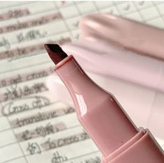 a pink pen sitting on top of a piece of paper with writing in the background