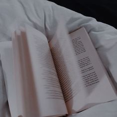 an open book sitting on top of a bed next to a white comforter and pillows