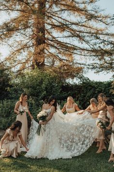 a group of women standing around each other on top of a grass covered field with trees in the background