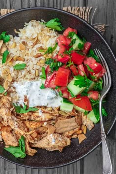 a black plate topped with rice, meat and veggies next to a fork