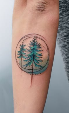 a small tattoo on the arm of a man with pine trees in a snow globe