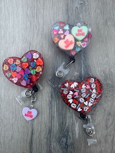 three heart shaped key chains are shown on a wooden surface with the words be mine written on them