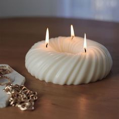 two white candles sitting on top of a wooden table next to a piece of jewelry