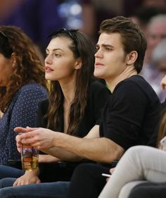 two people sitting next to each other at a basketball game, one holding a bottle