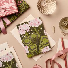 some cards with pink flowers and green leaves are on a table next to other items