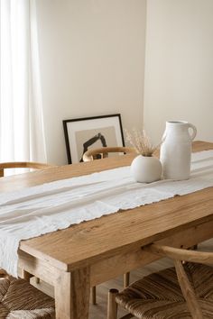 a white vase sitting on top of a wooden table next to two chairs and a framed photograph