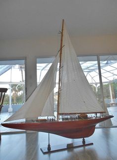 a model sailboat sitting on top of a hard wood floor in front of large windows