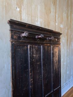 an old black cabinet with knobs on the top and bottom is against a wall