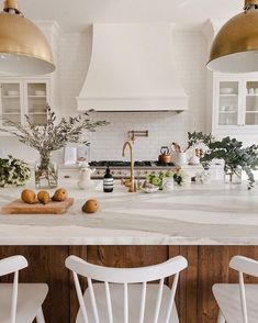 a kitchen with white counter tops and gold pendant lights over the sink, along with three chairs