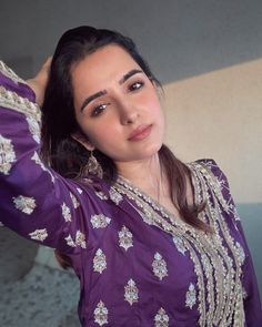 a woman in a purple dress posing for the camera with her hand on her head