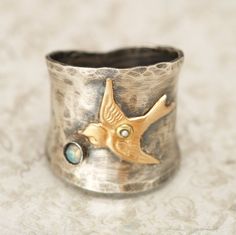 "This wide band ring was inspired by nature and also works great as a thumb ring! The wide sterling silver band has a gently hammered texture and is oxidized and then hand buffed to show highlights. Accenting the sterling silver ring is a 14kt gold filled bird or swallow. The center of the bird is embellished with a tiny real pearl! Below the bird is a place for your choice of a Czech cabochon. Please choose the color you would like from the personalize option. The is set in a 925 sterling silve Silver Bird Ring, Bird Watcher Gifts, Sterling Silver Opal Ring, Bird Ring, Bird Rings, Unique Opal, Silver Opal Ring, Wedding Bands For Her, Hammered Silver Ring