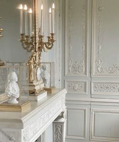 a white mantle with candles and figurines on it in front of a mirror