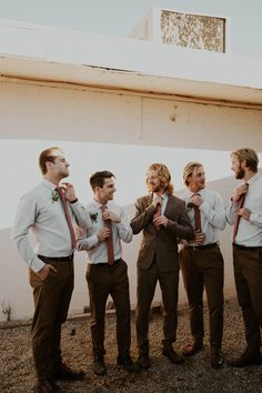 a group of men standing next to each other in front of a building with ties on