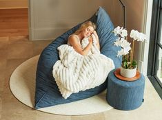 a woman laying on a bean bag chair with a blanket over her face and flowers in the corner