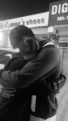 a man is hugging another man in front of a store sign at night with his arms around him