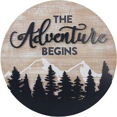 the adventure begins sign with trees and mountains in the background on a wooden plaque that says,