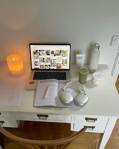 an open laptop computer sitting on top of a white desk next to a lit candle