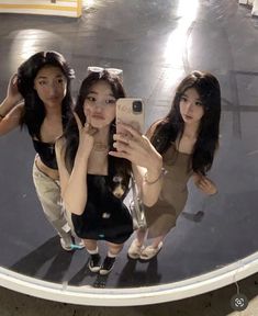 three young women taking a selfie in front of a mirror with their cell phones