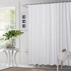 a white shower curtain in a bathroom next to a table with a potted plant