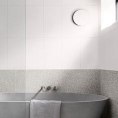 a bath tub sitting under a window next to a white tiled wall and floor in a bathroom