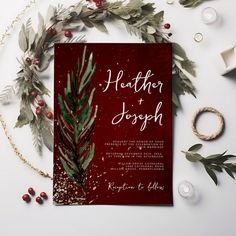 a red wedding card with greenery and berries on the front is surrounded by other holiday decorations