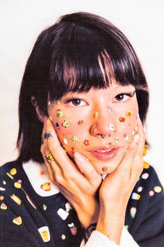 a woman with sprinkles on her face and hands near her face looking at the camera