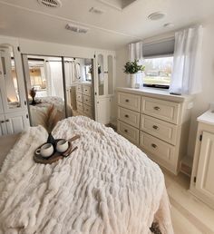 a white bed sitting in a bedroom next to a dresser under a window with two pairs of shoes on top of it