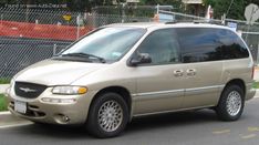 a beige minivan is parked on the side of the road in front of a fence