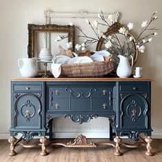 a blue dresser with white flowers and vases sitting on it's sideboard