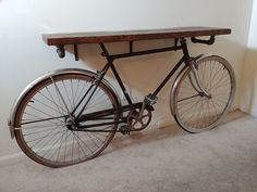 an old fashioned bicycle sitting under a wooden table on carpeted floor next to white wall